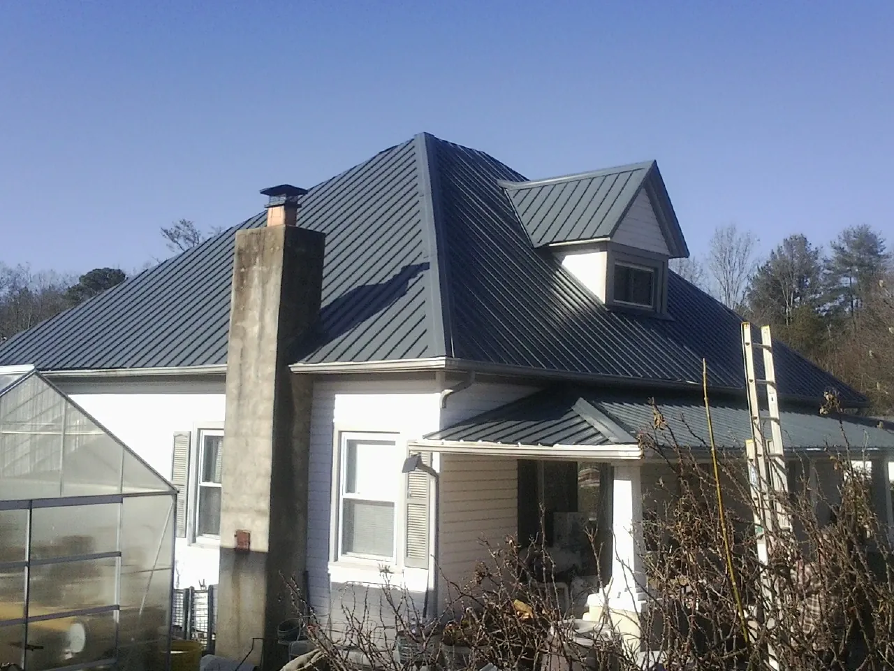 Dark blue standing seam metal roof on a white farmhouse with dormer — Slate & Tile Roof Repair by Roofing Brothers in Harlingen