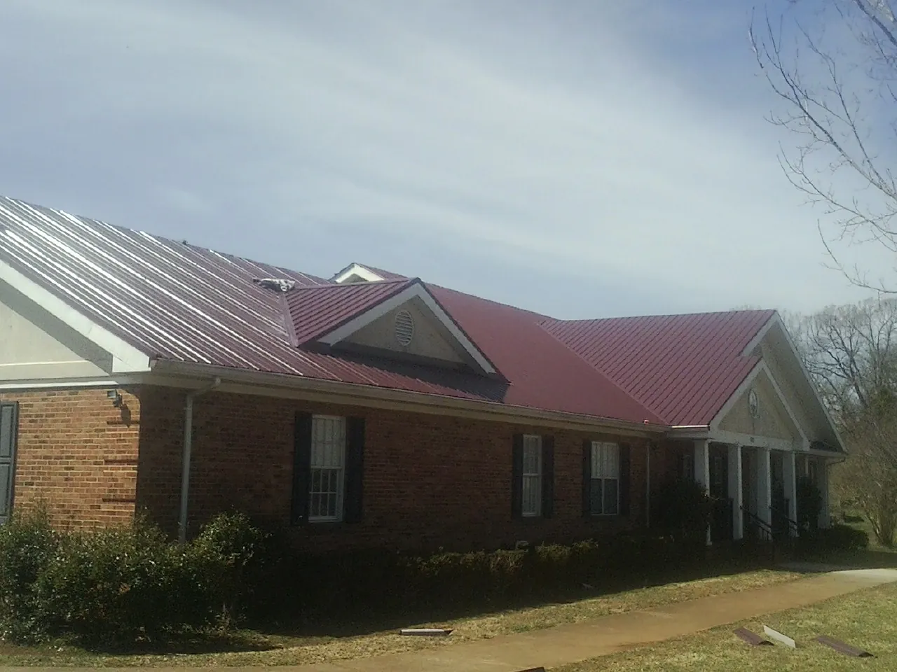 Red metal roof with gabled entries on a long brick building, from a Hail Damage Roof Repair job in Harlingen