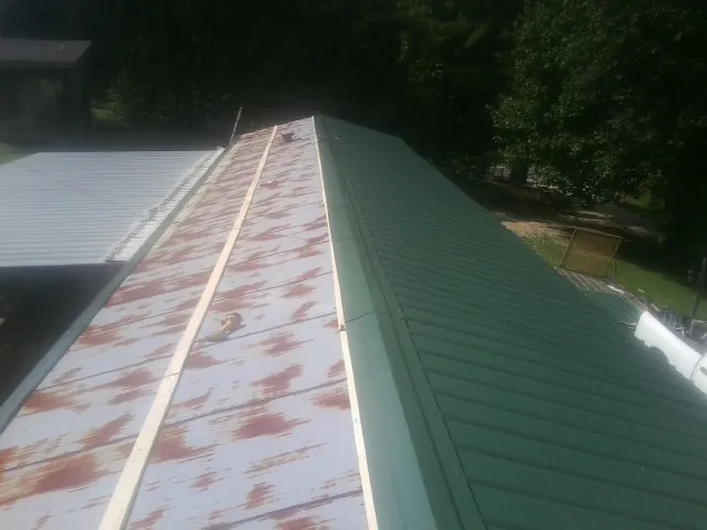 Old rusted panels beside newly installed green metal roofing — Wind Damage Roof Repair by Roofing Brothers in Harlingen