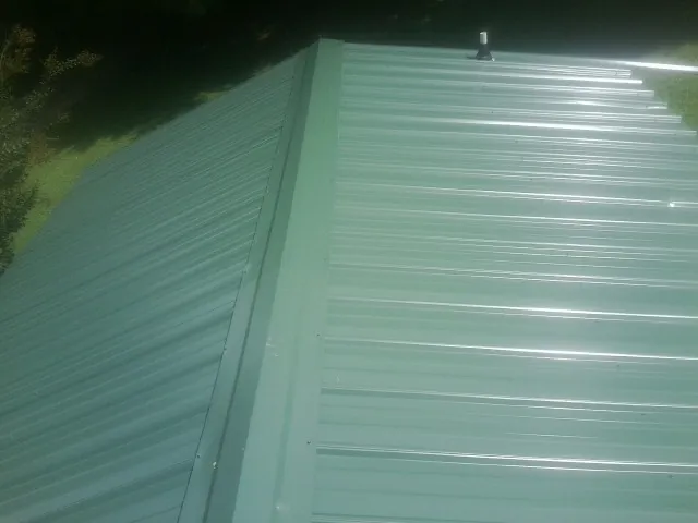 New green metal panels meeting at the ridge of a roof — Flat Roof Repair work by our crew in Harlingen