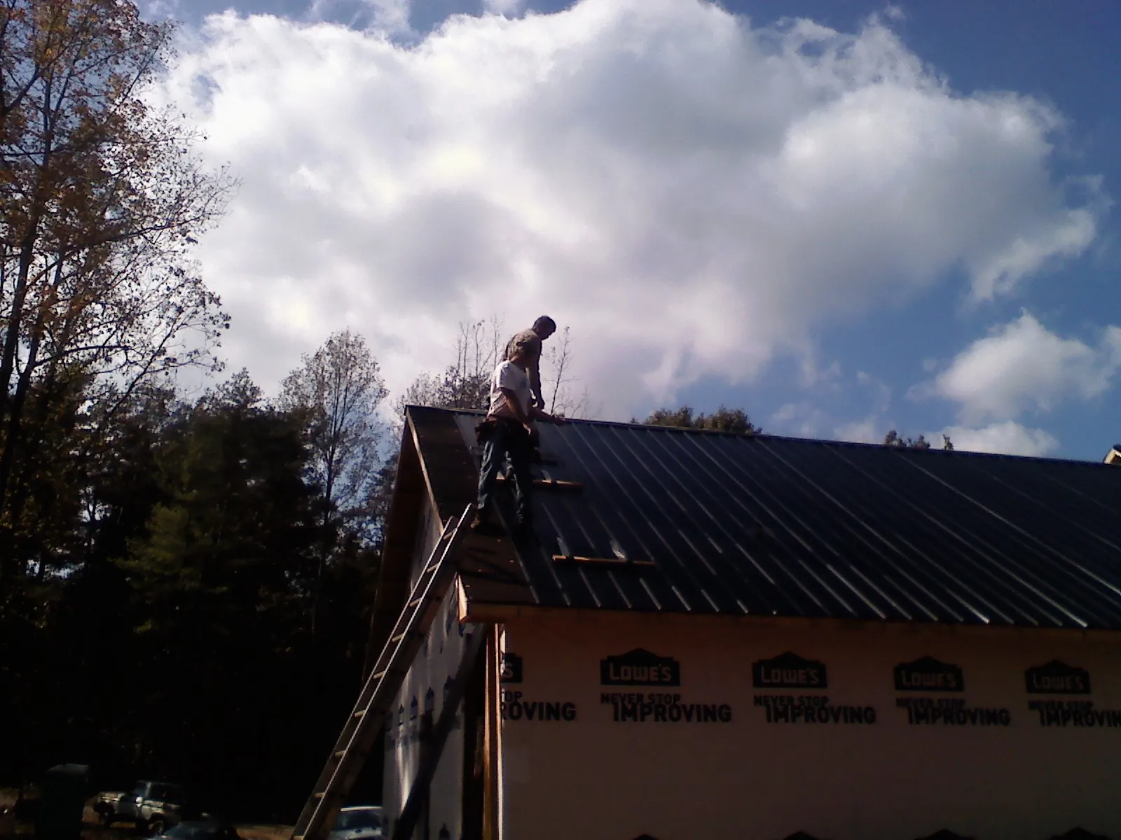 Roofer fastening dark metal panels high against a cloudy sky, from a Roof Inspection job in Harlingen