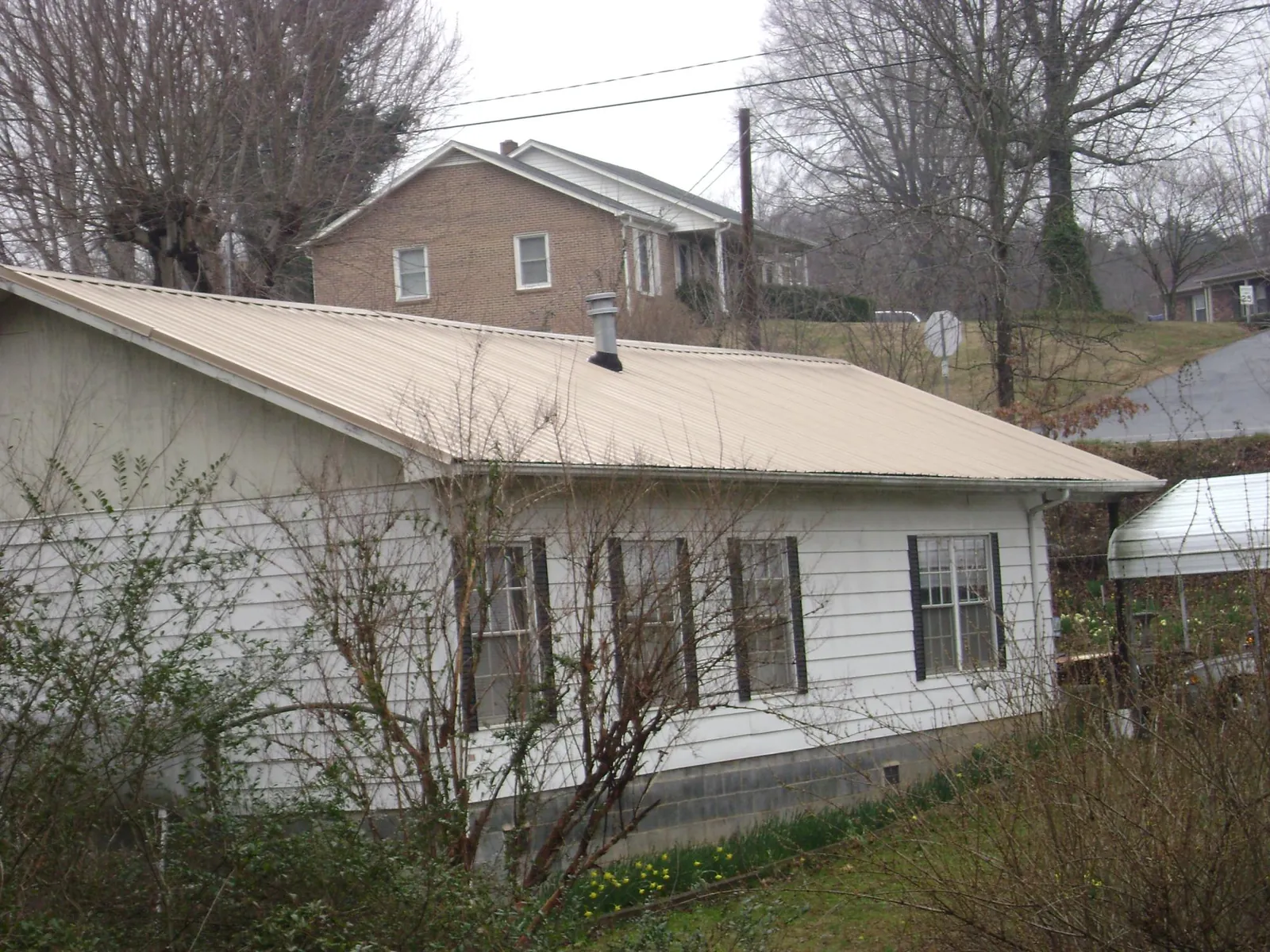 Tan metal roof on a white sided house set into a hillside — Commercial Roofing by Roofing Brothers in Harlingen